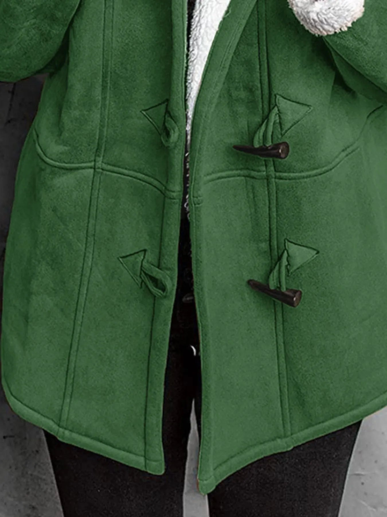 Close-up of a cozy green sherpa lined toggle coat with two front pockets.