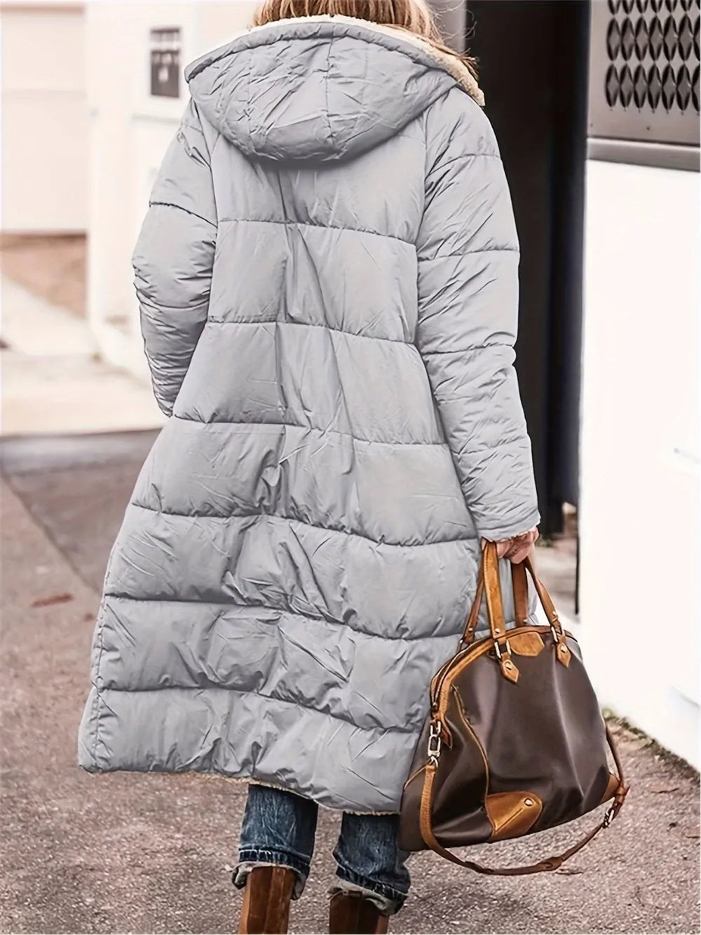 Back view of a woman in a grey full-size zip-up Sherpa hooded coat, holding a brown handbag.