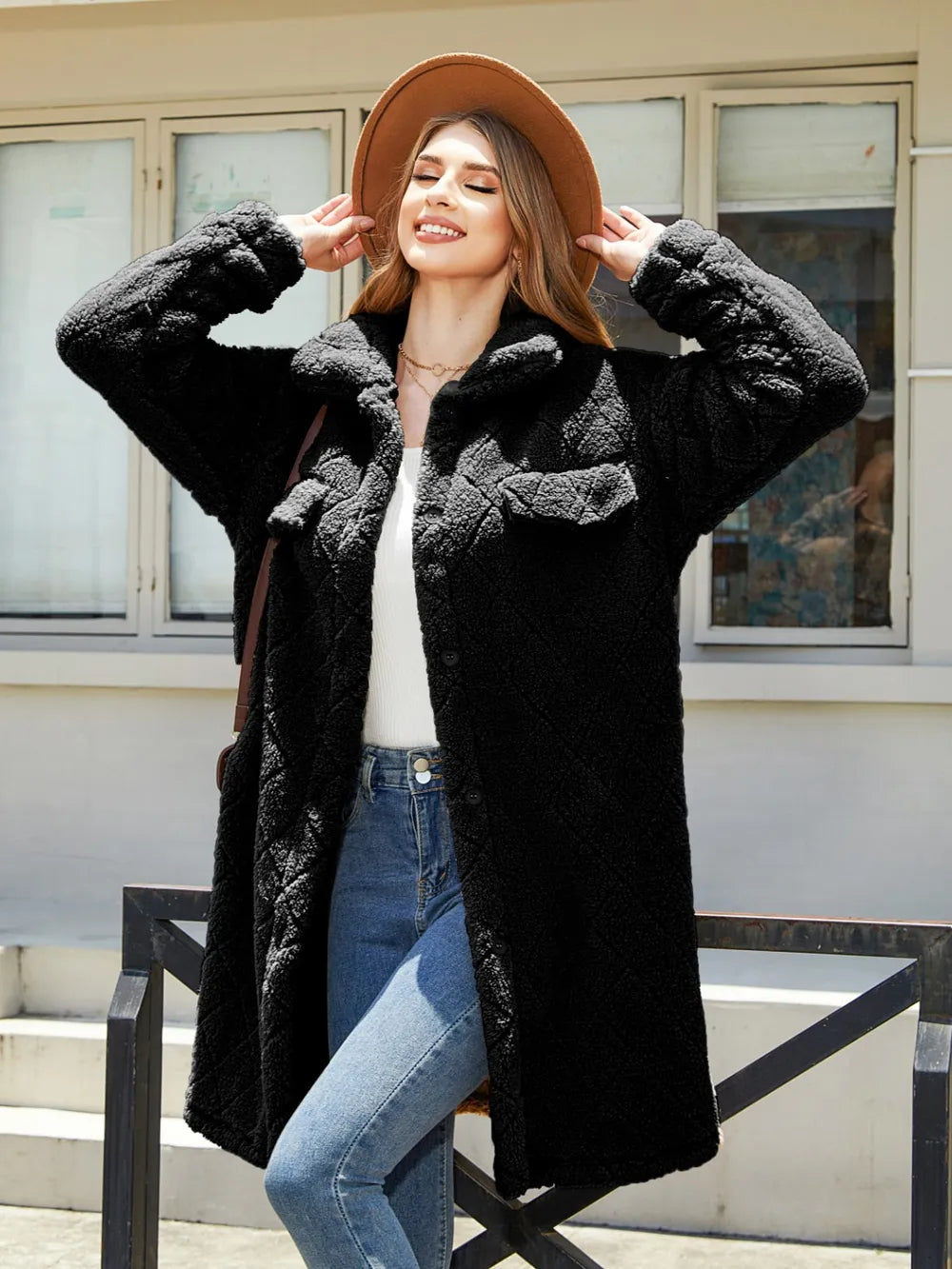 Model wearing a black texture button up coat with dropped shoulders, posing outdoors with a hat and casual attire.