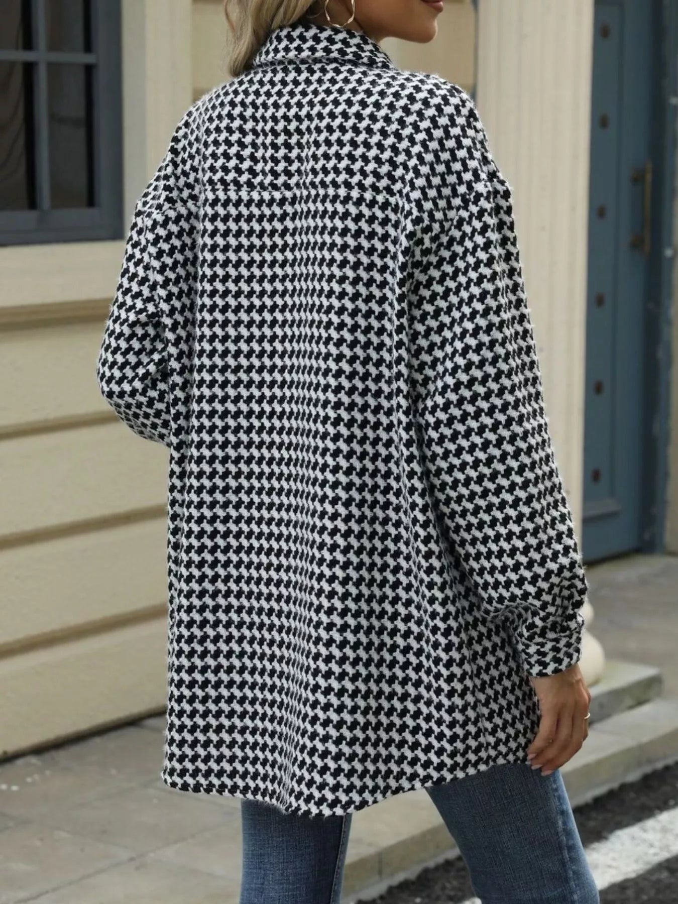 Back view of a houndstooth button-up long sleeve coat in black and white, paired with casual denim jeans.