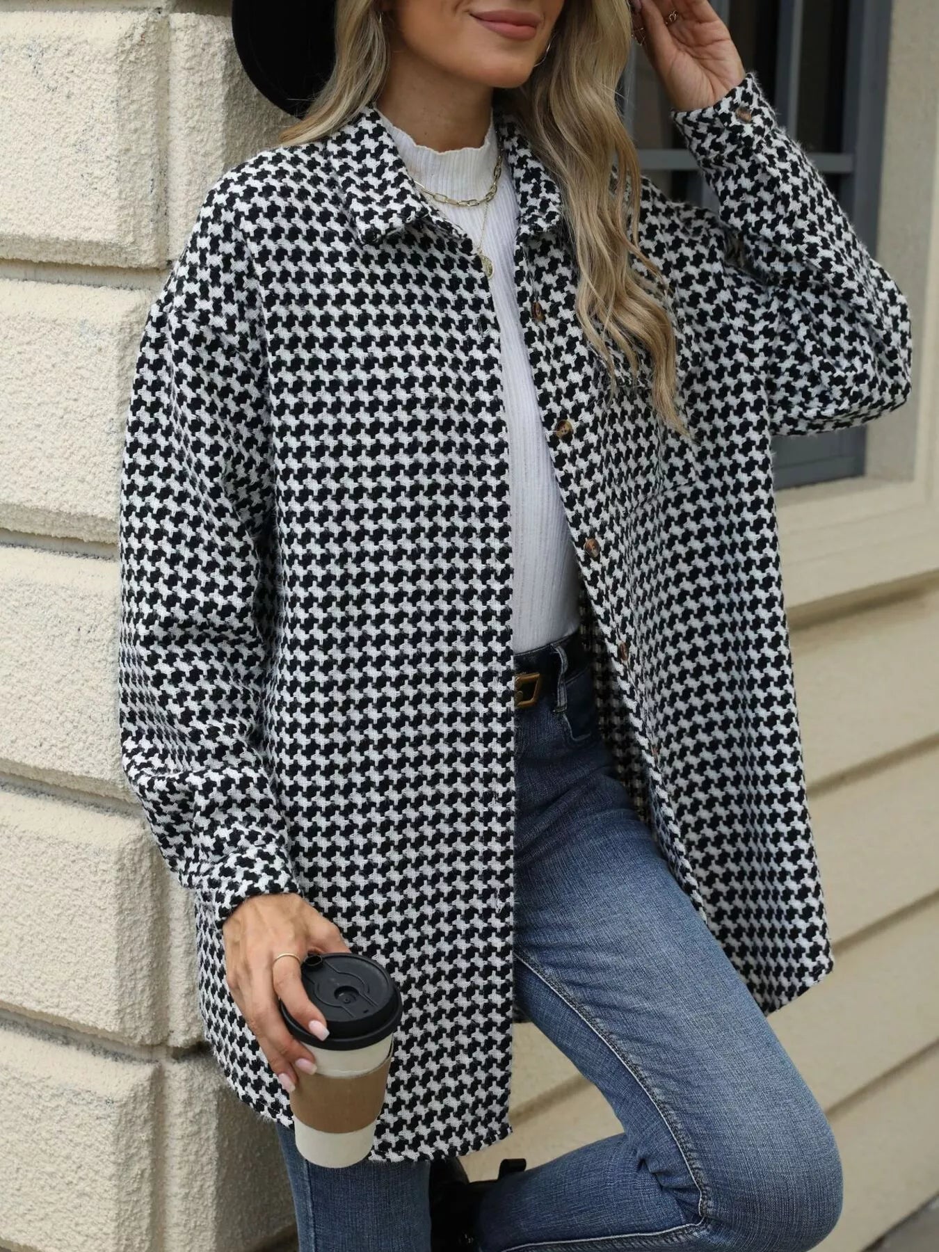 Woman wearing a houndstooth button-up long sleeve coat, holding a coffee cup.
