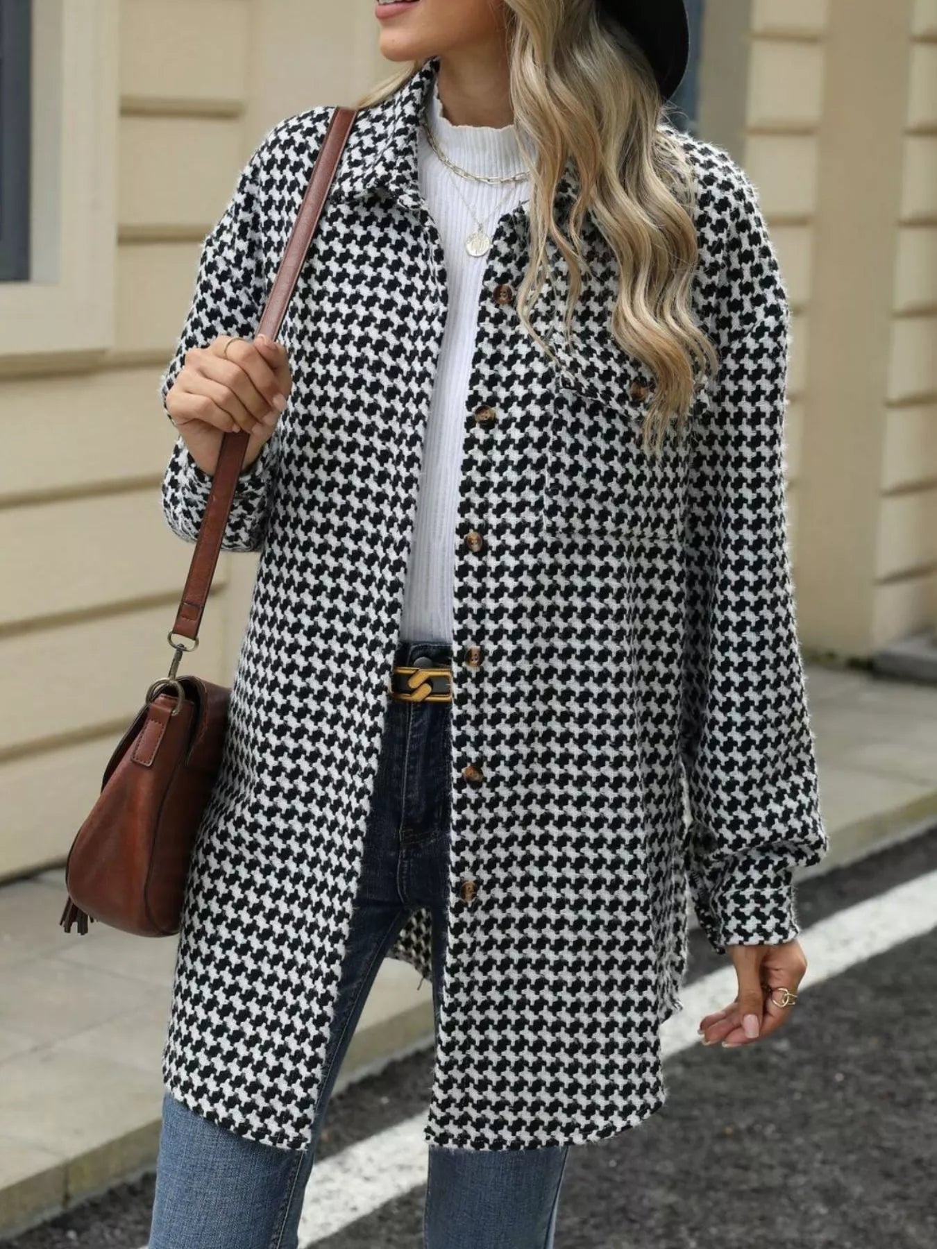 Woman wearing a houndstooth button-up long sleeve coat with a white sweater and jeans, holding a brown handbag.