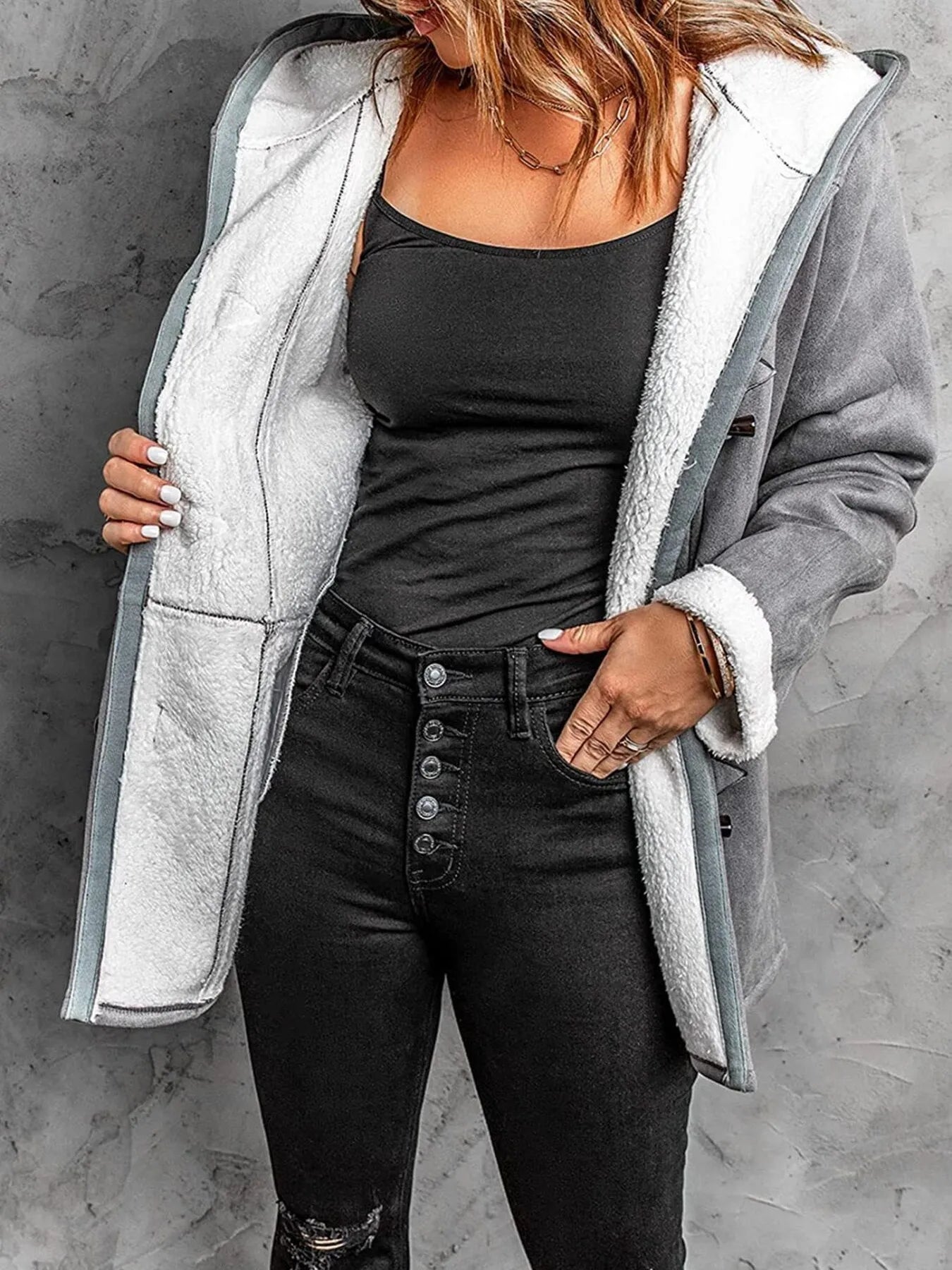 Model wearing a cozy sherpa lined toggle coat with hood, paired with a black tank top and high-waisted jeans.