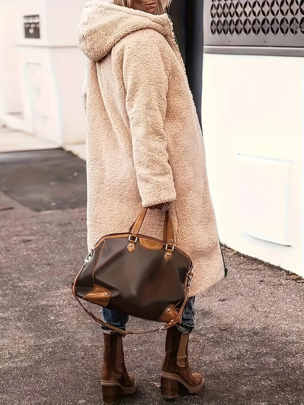 Woman in a cozy beige zip-up sherpa hooded coat, carrying a brown handbag, walking outdoors.