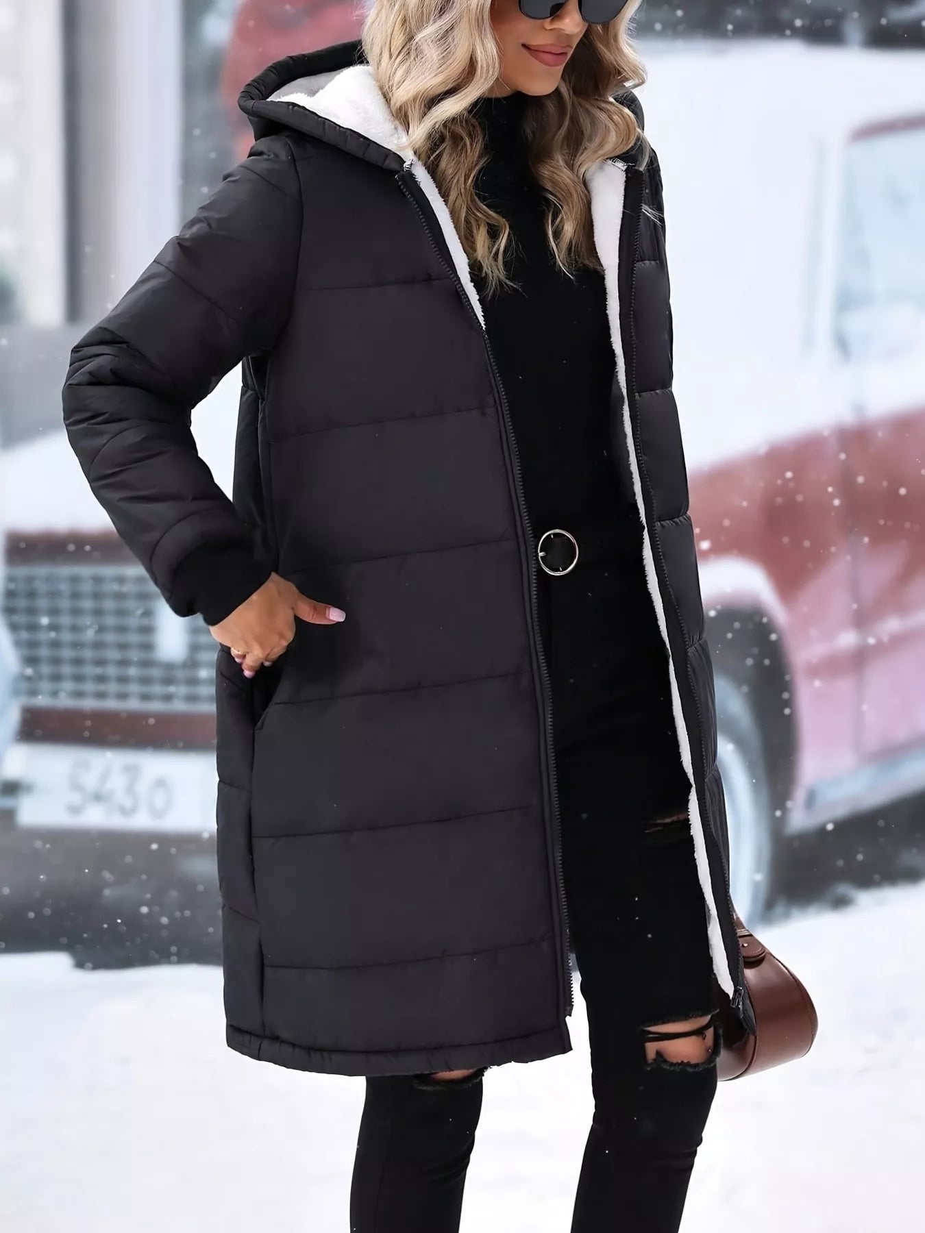Woman wearing a black quilted zip up puffer coat with hood, styled for winter fashion in a snowy setting.