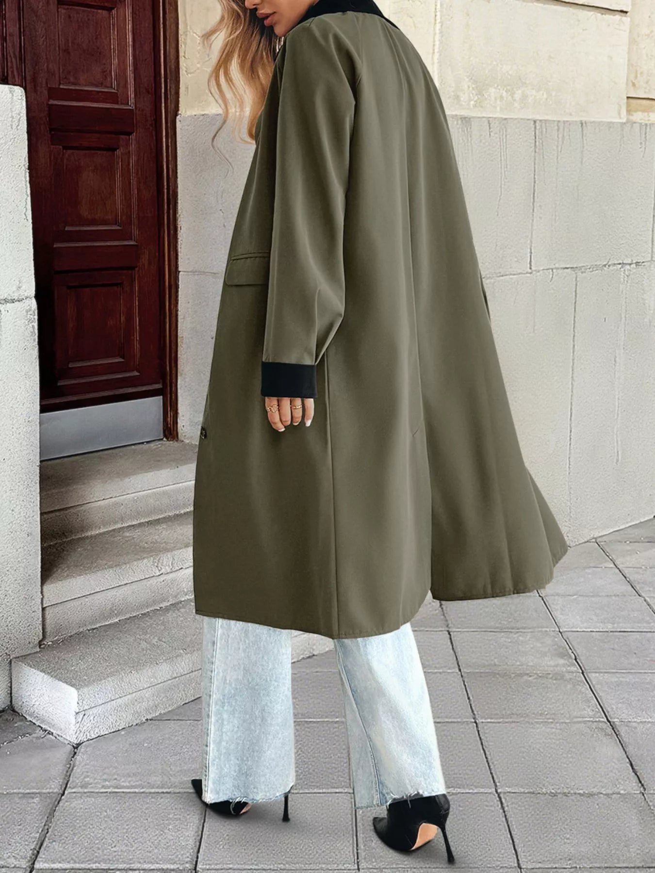 Back view of a woman wearing a contrast collar button-up coat, paired with stylish pants, standing on a stone pathway.