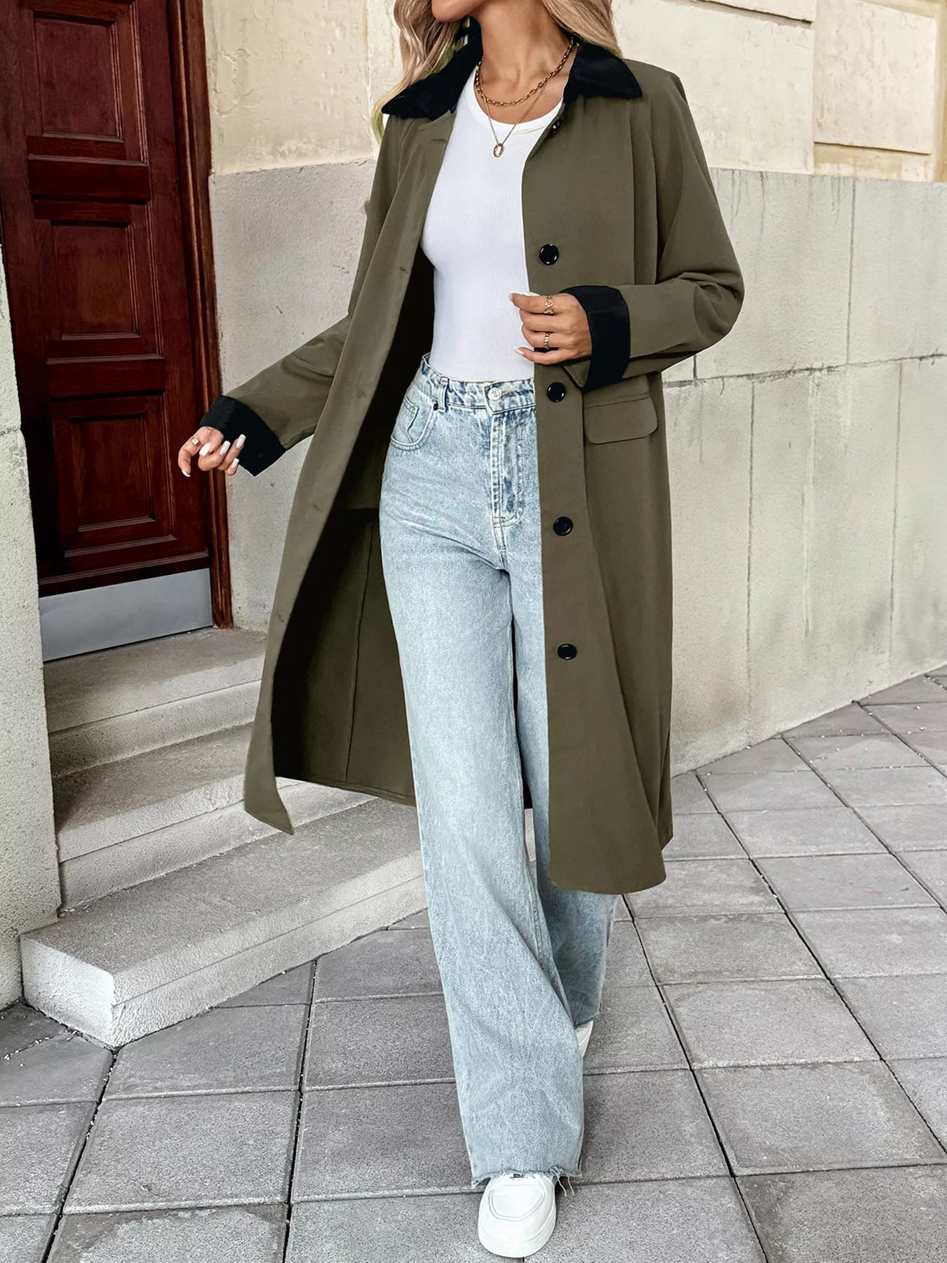 Woman wearing a contrast collar button-up coat with a white top and flared jeans, walking outdoors.