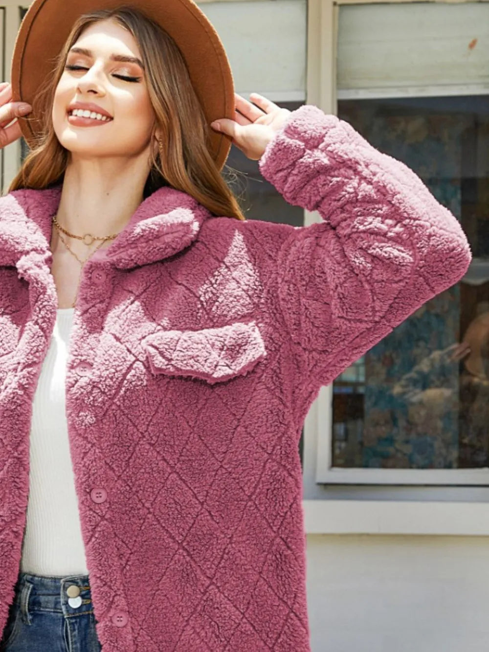 Model wearing a textured button-up coat in blush pink, posing outdoors with a friendly smile.