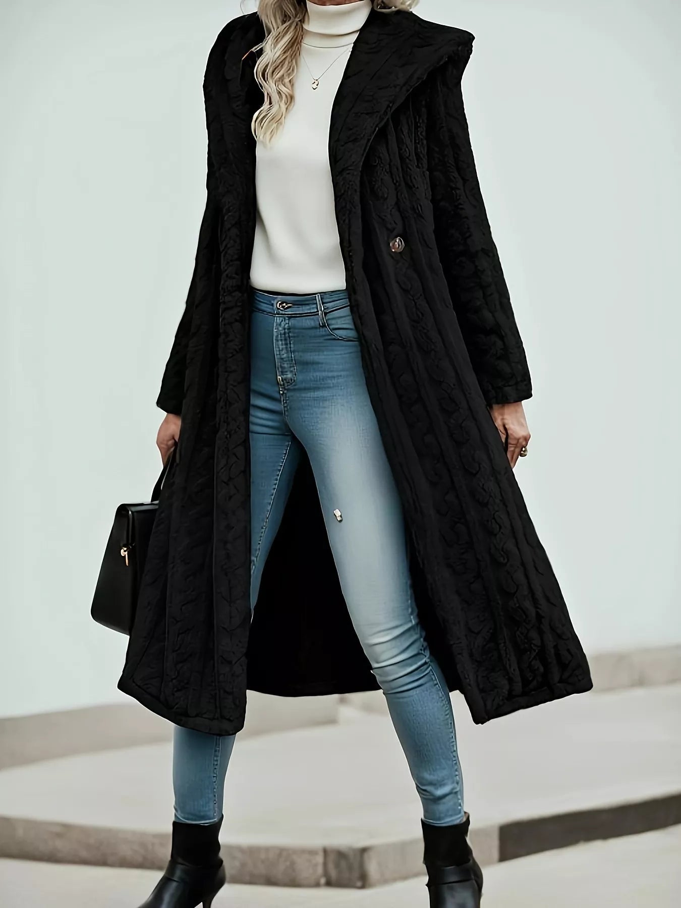 Black Sherpa longline hooded coat featuring buttoned front and thick material, styled with jeans and a turtleneck.
