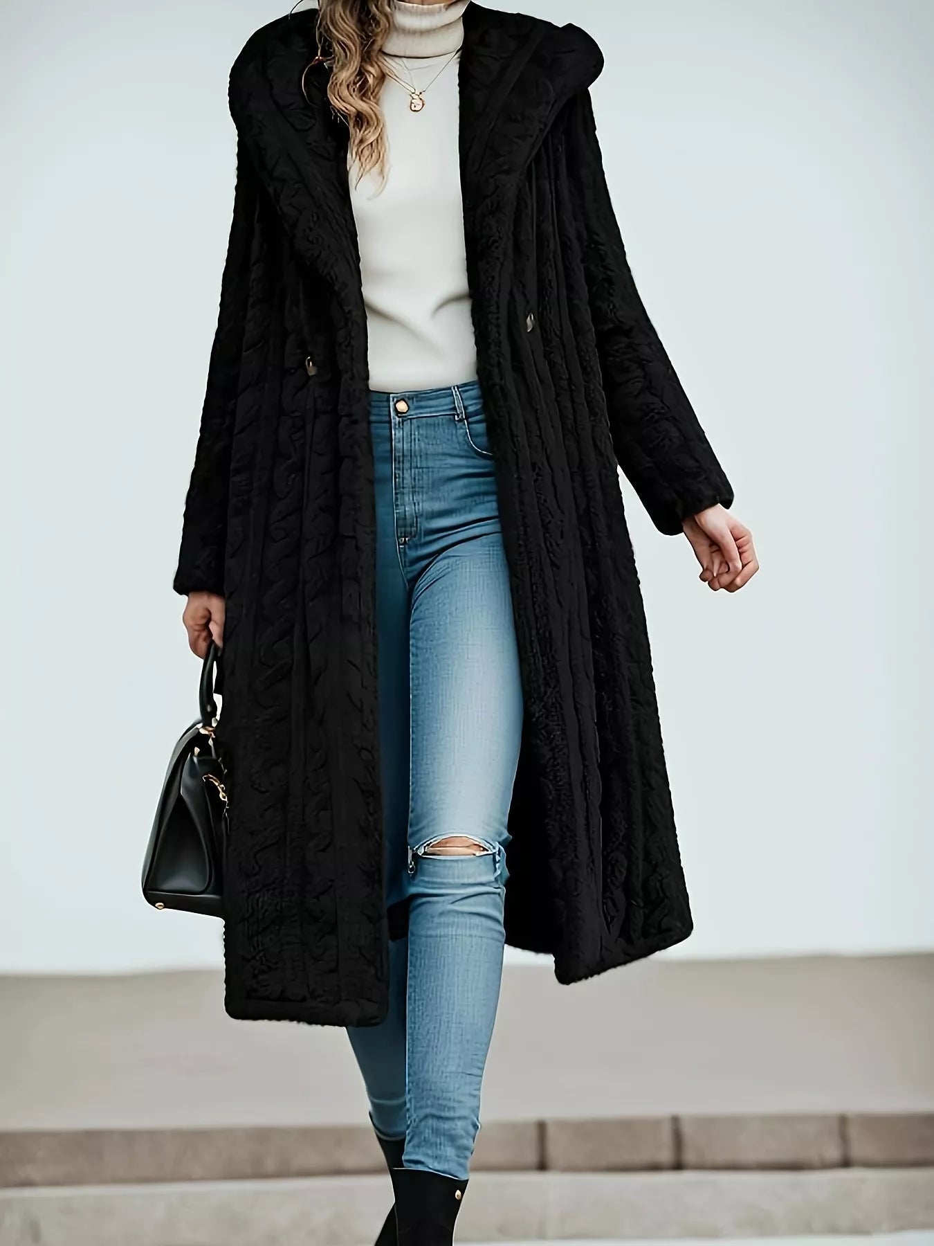 Woman wearing a black Sherpa longline hooded coat over a stylish outfit with jeans and a top, showcasing a trendy look.