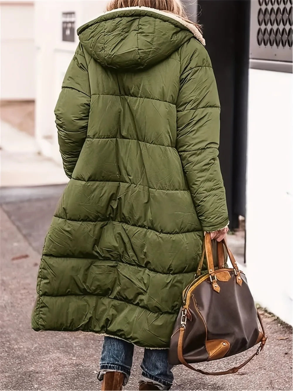 Woman wearing an olive green zip-up sherpa hooded coat, carrying a brown handbag, on a city street.